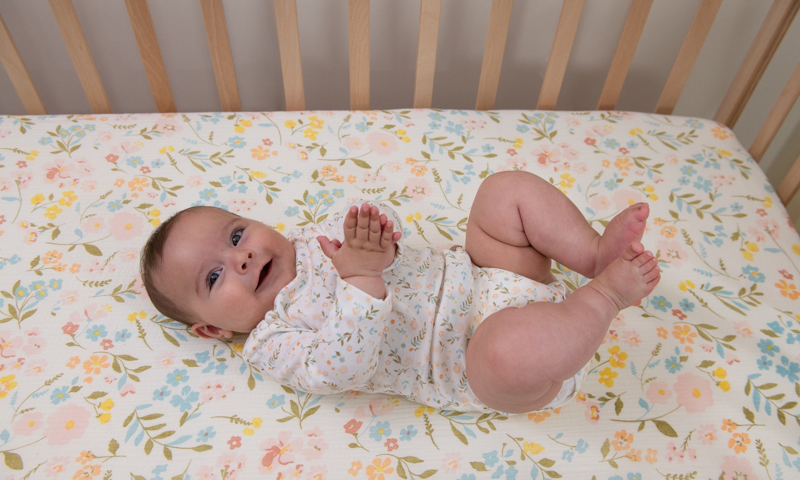 A joyful baby laying on muslin flower-themed crib sheets.