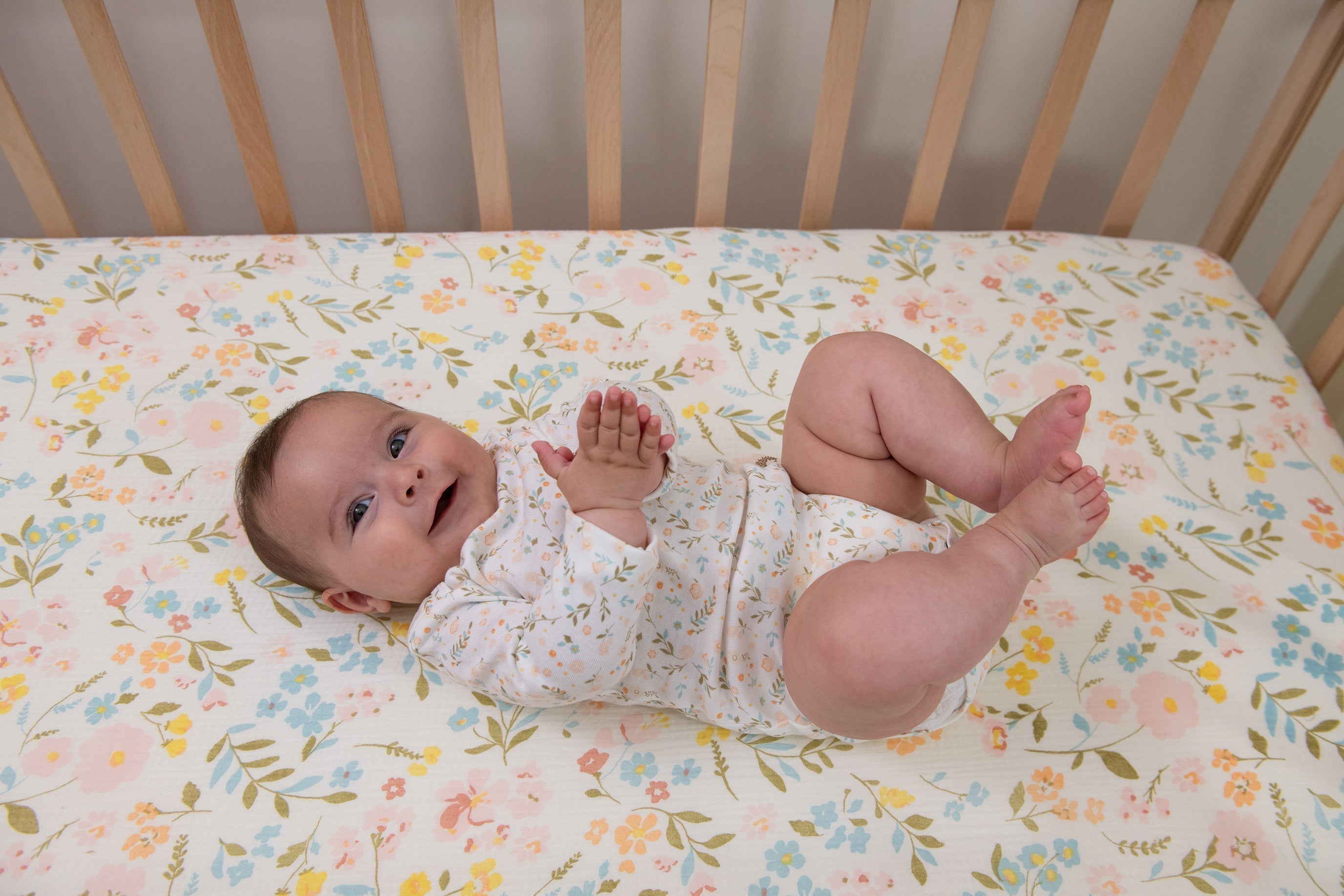 A joyful baby laying on muslin flower-themed crib sheets.