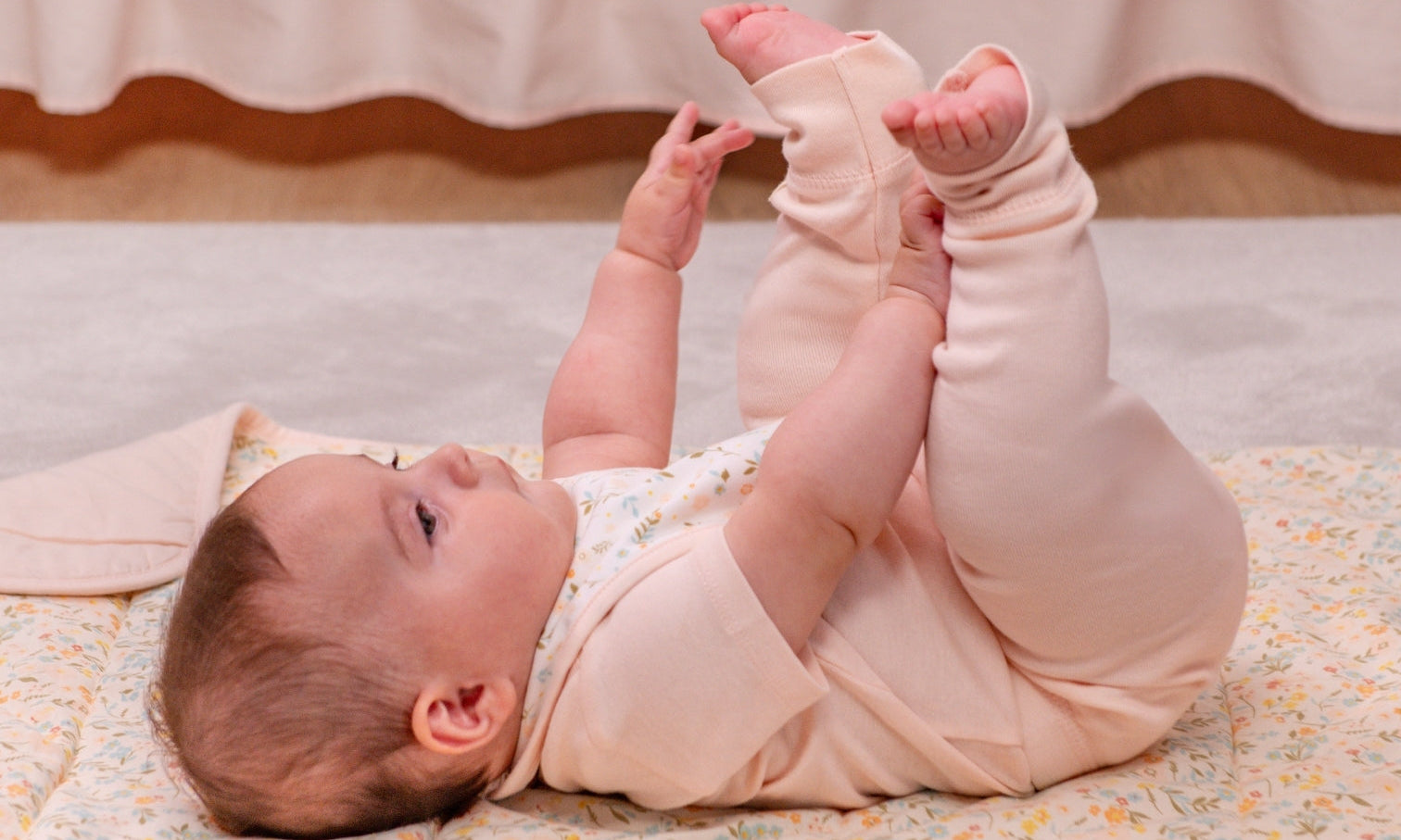 Smiling baby in a pink short-sleeve onesie lying on a pink organic blanket