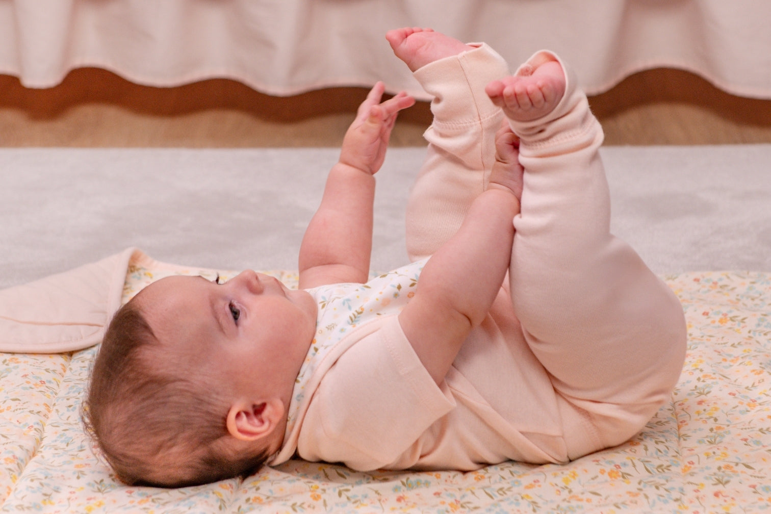 Smiling baby in a pink short-sleeve onesie lying on a pink organic blanket