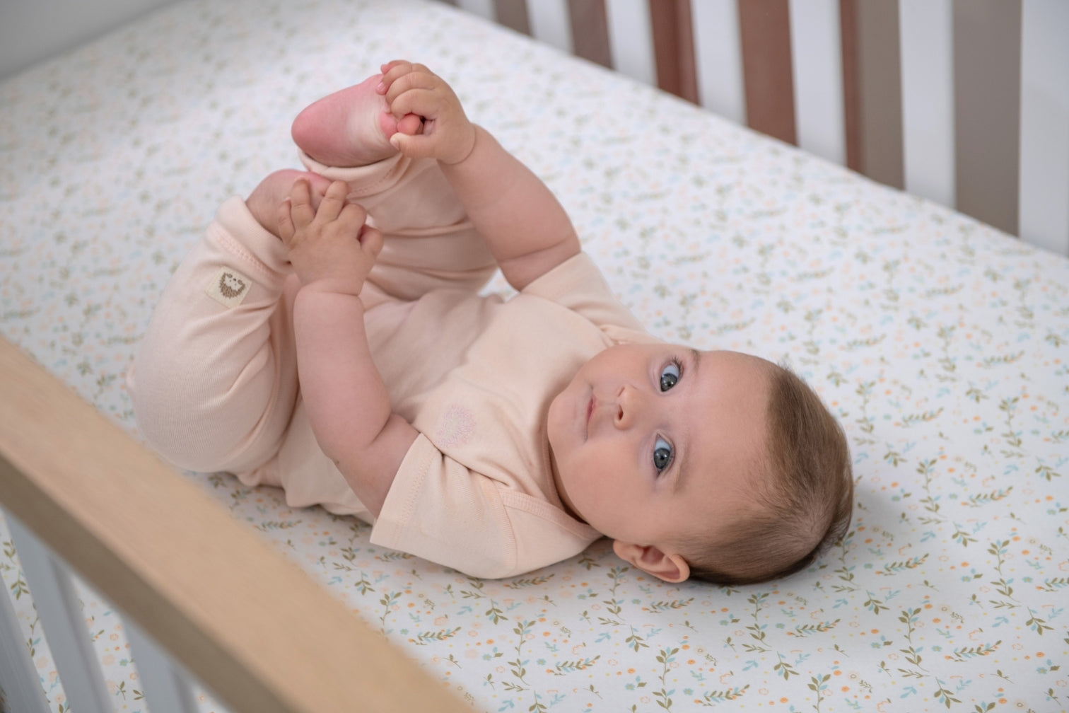 baby wearing pink short-sleeve onesie laying on a floral crib sheet