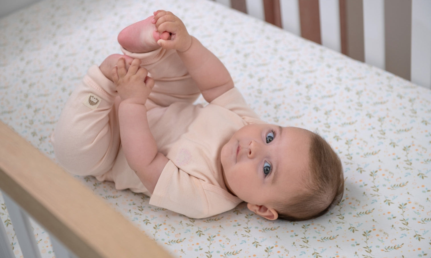 baby wearing pink short-sleeve onesie laying on a floral crib sheet