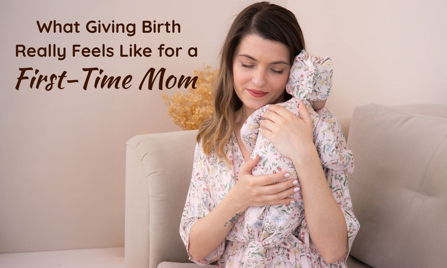 a new mother in a botanical maternity dress gently cradling her swaddled newborn while sitting on a couch