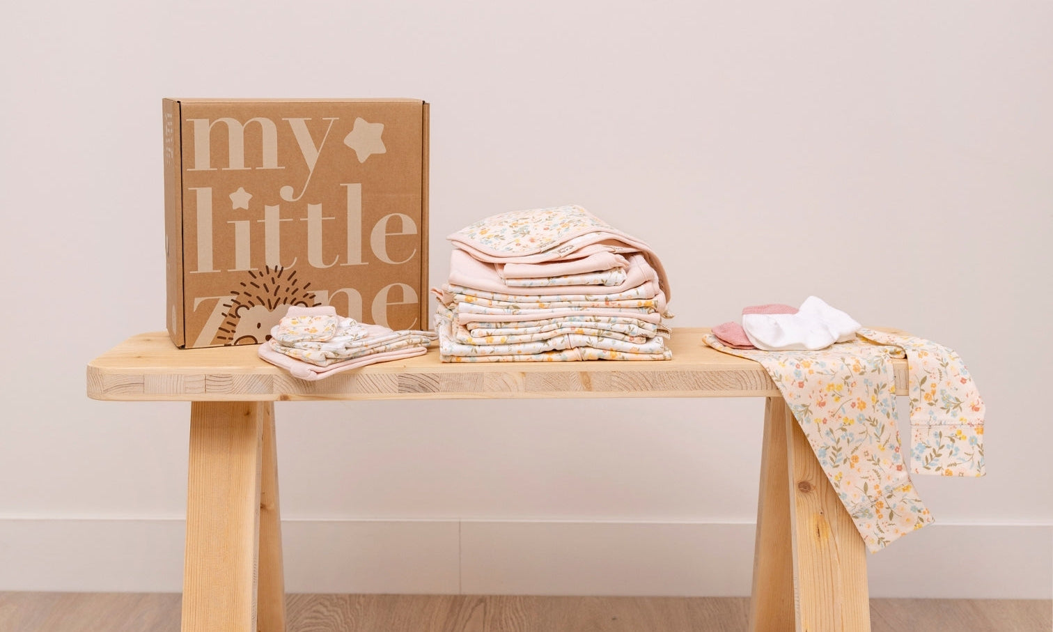 My Little Zone floral baby layette set neatly folded on a wooden bench with branded gift box