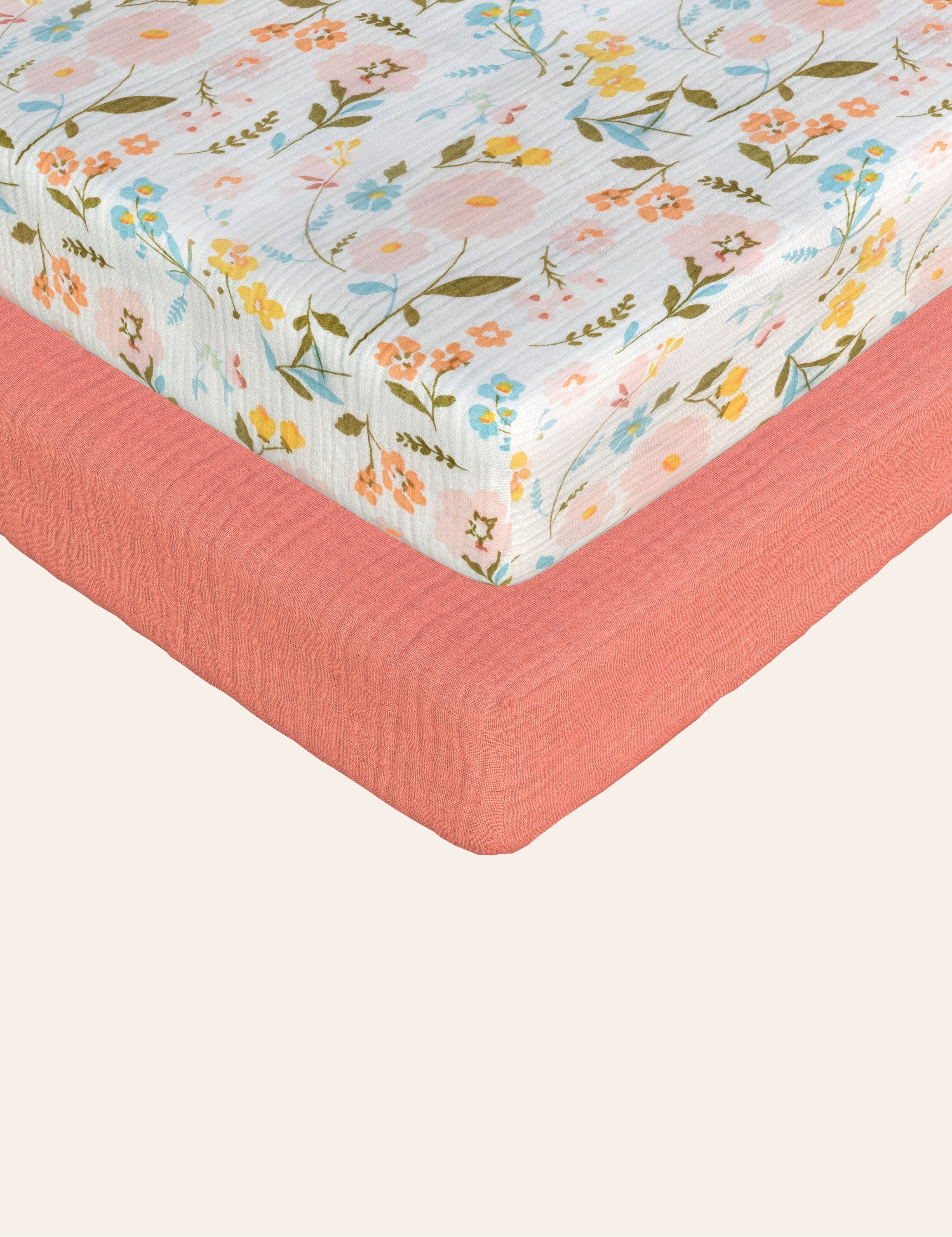 Muslin Floral patterned pack n play sheet with a muslin solid coral pack n play sheet on a white background