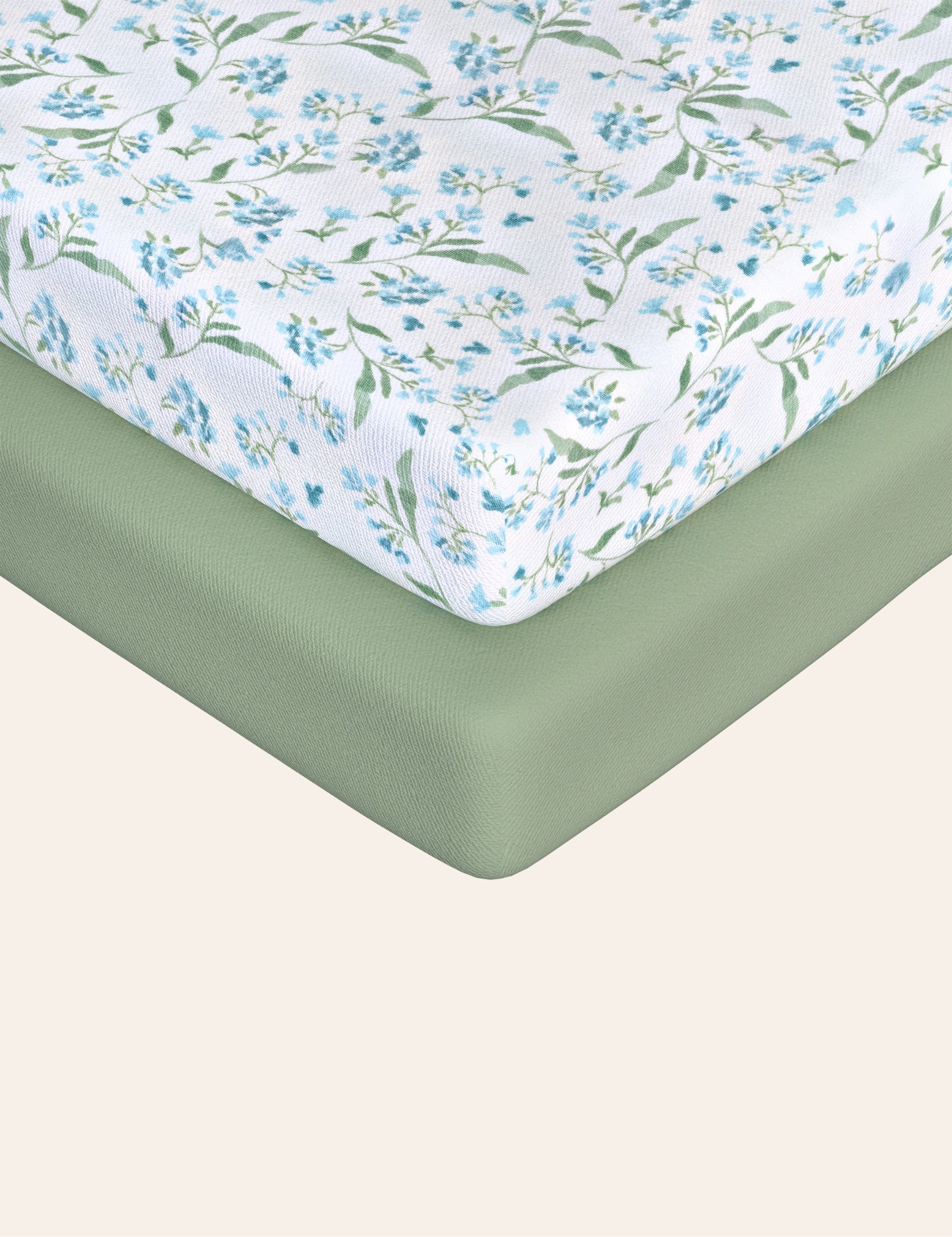 A fitted sheet with a floral pattern and a solid green fitted sheet are placed on a mattress.