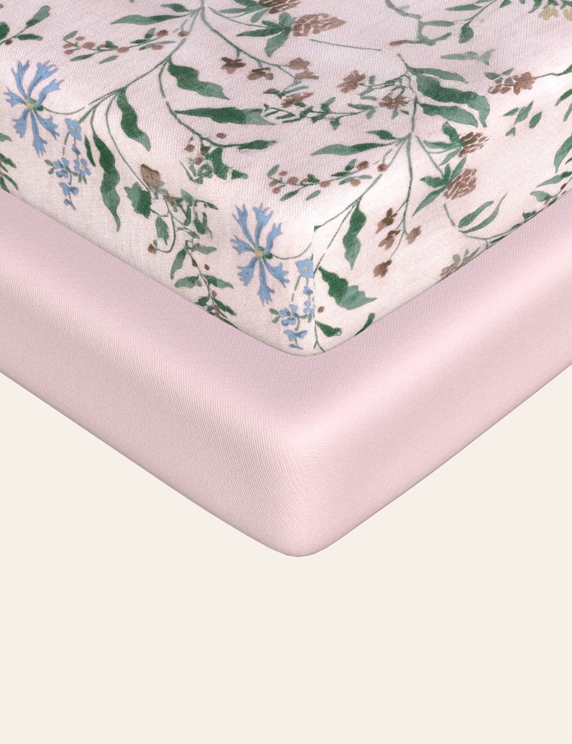A fitted sheet with a floral pattern and a solid pink fitted sheet are placed on a mattress.