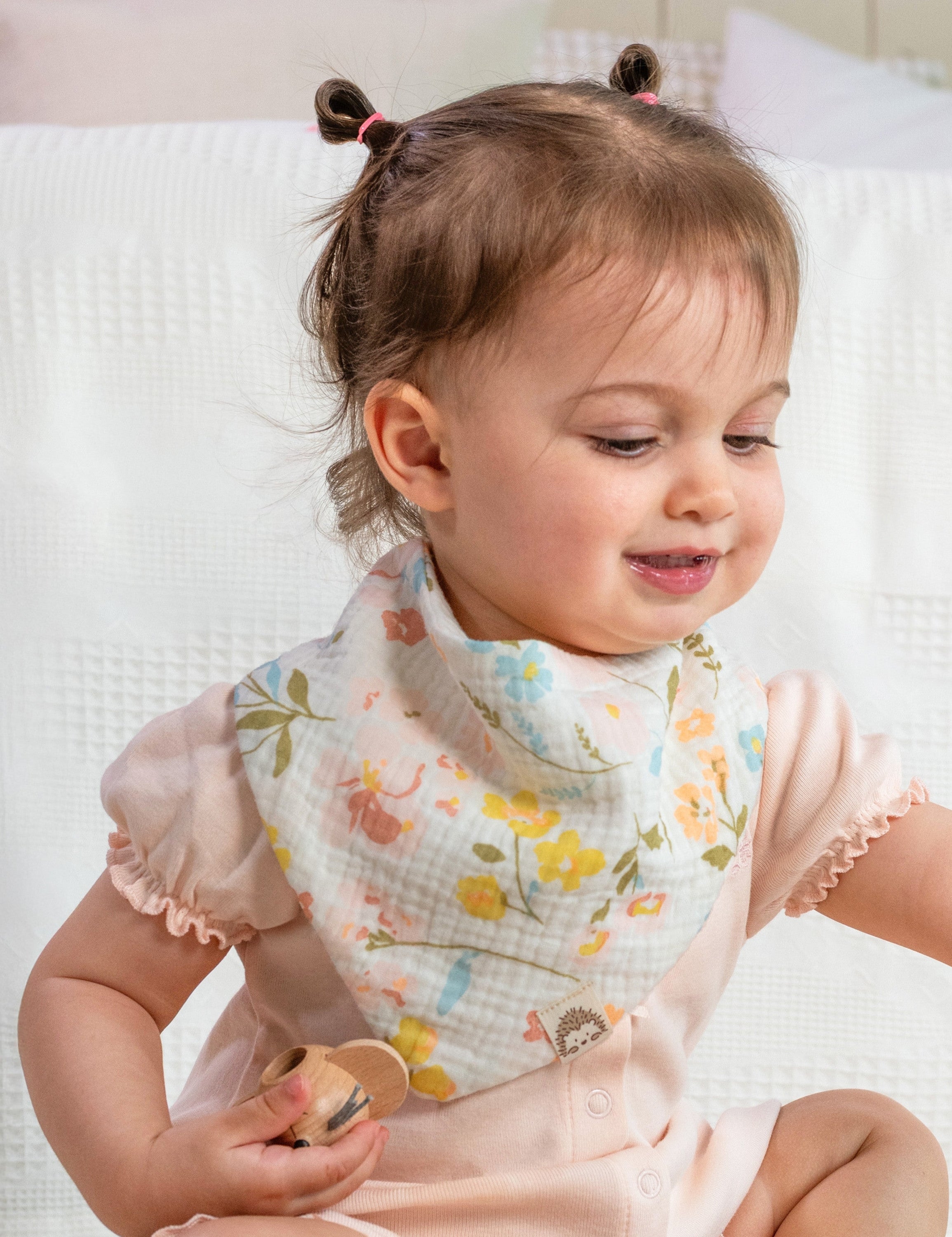 Baby wearing a floral-patterned muslin bandana bib over a solid pink romper
