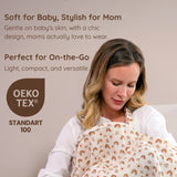 Mother holding her baby wrapped in a rainbow patterned muslin nursing cover with text about product features and OEKO-TEX certification.