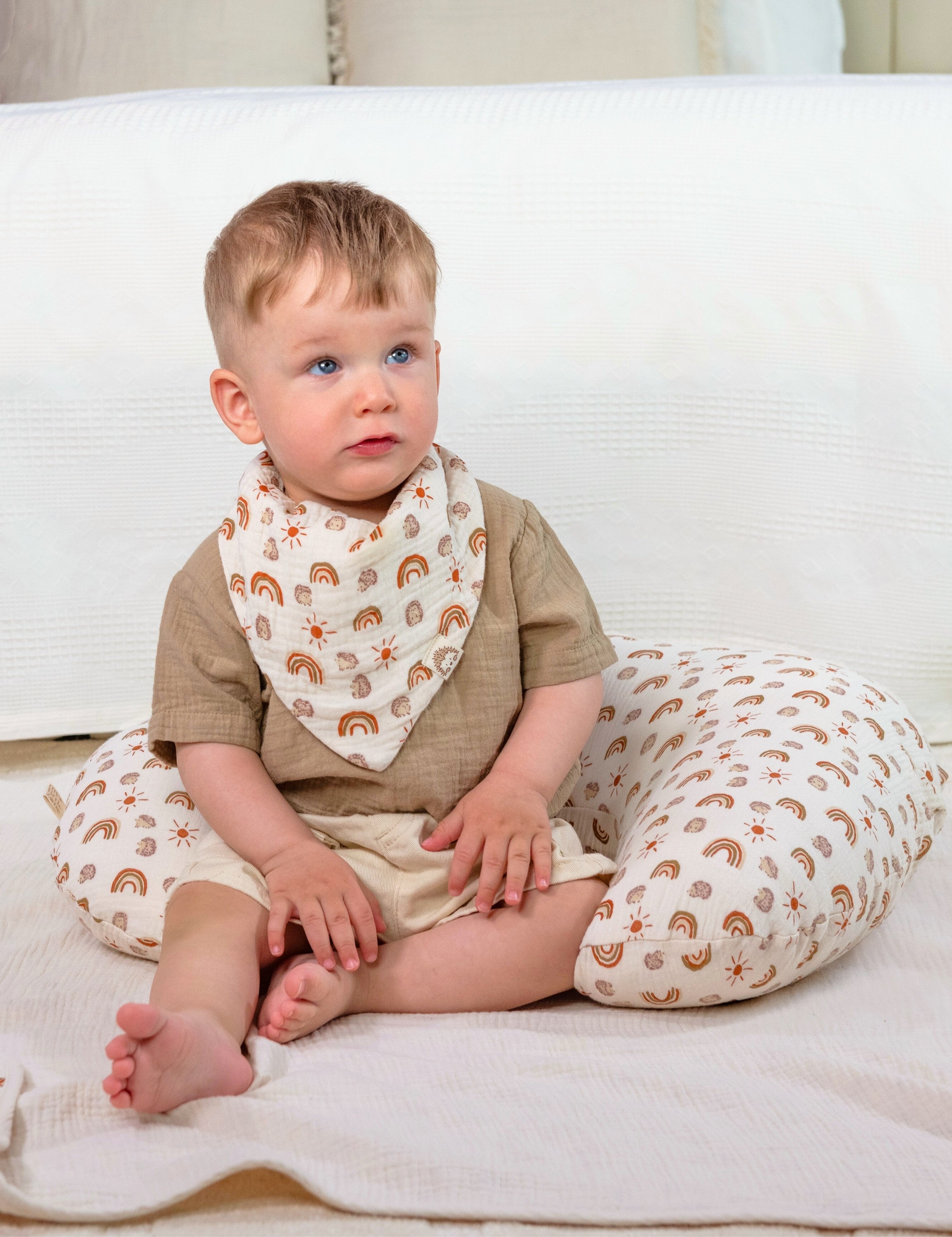 Child sitting on a rainbow patterned muslin nursing pillow