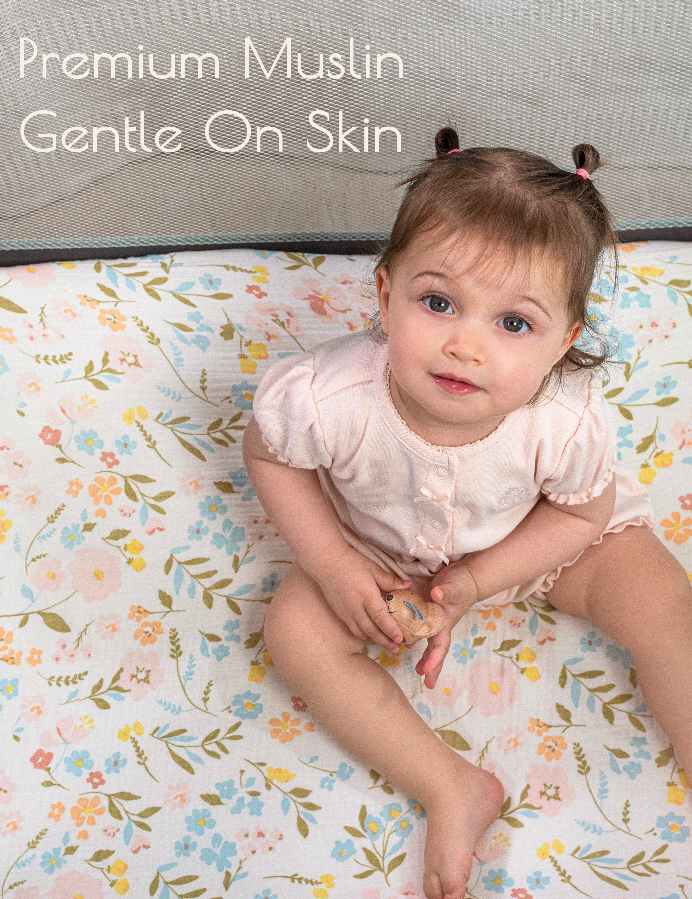 Baby sitting in a pack n play crib with floral patterned muslin pack n play fitted sheet.