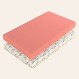 Two pack n play mattresses, one solid coral and one with a floral patterned design, on a light beige background.
