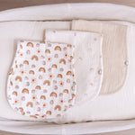 Three muslin burp cloths with different patterns displayed on a bassinet basket.