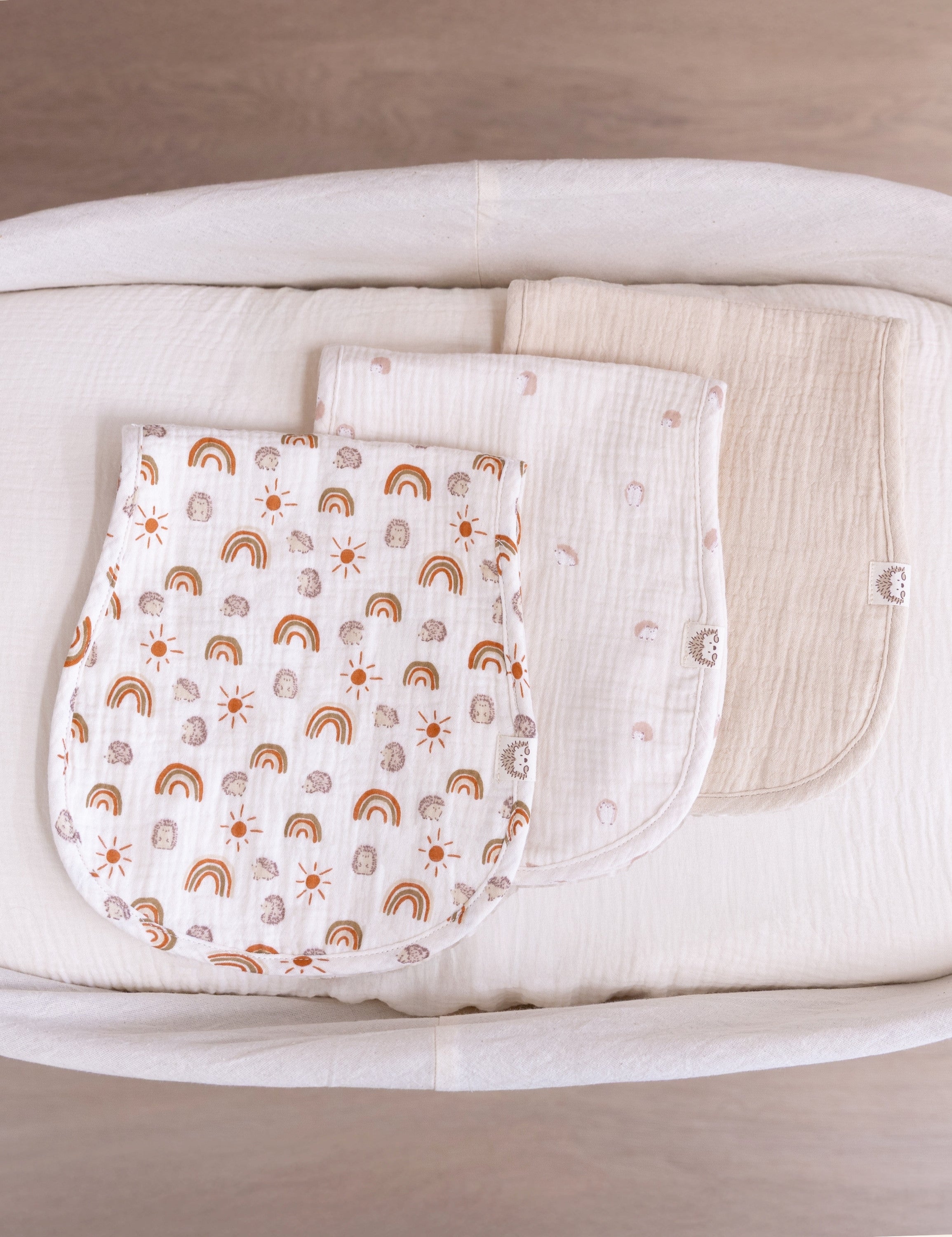 Three muslin burp cloths with different patterns displayed on a bassinet basket.