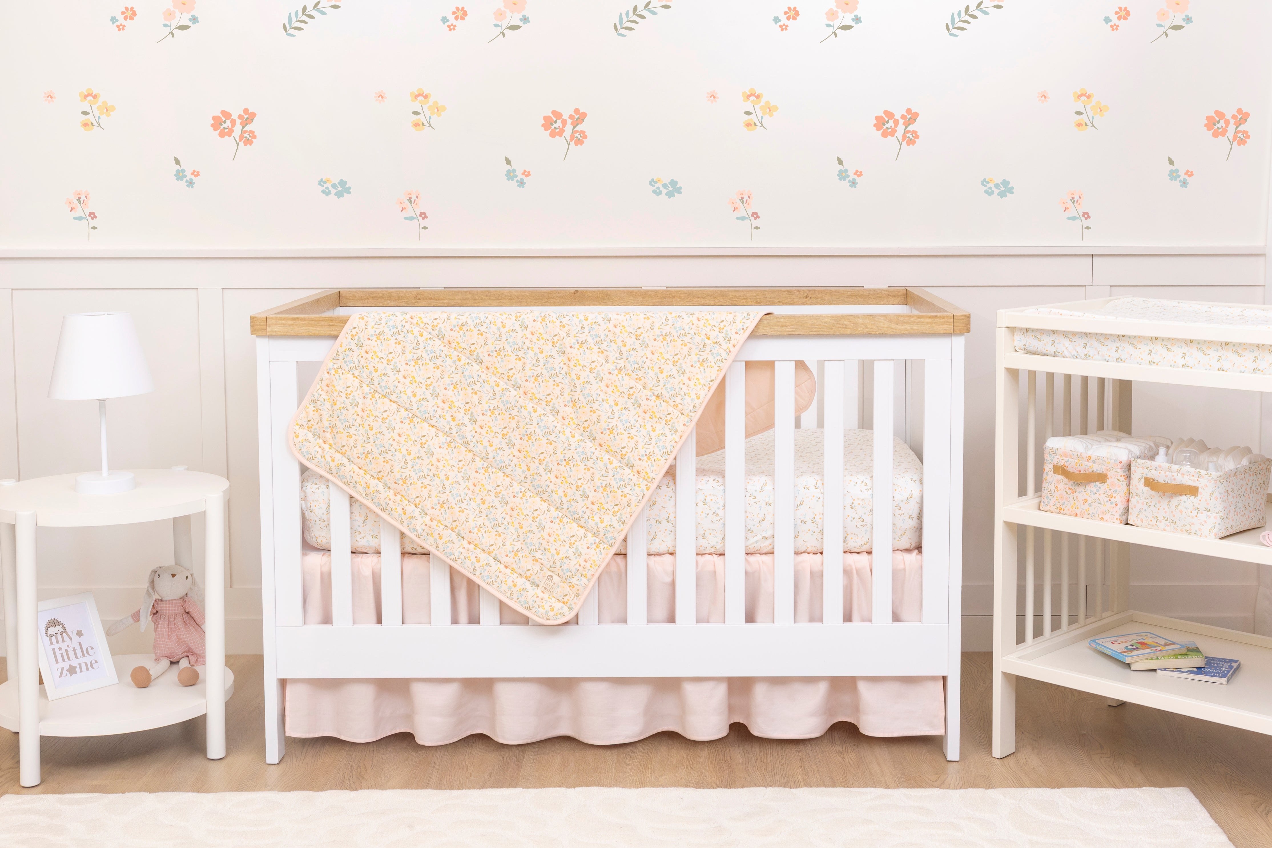 Nursery room with a white crib and changing table against a floral wallpapered wall.